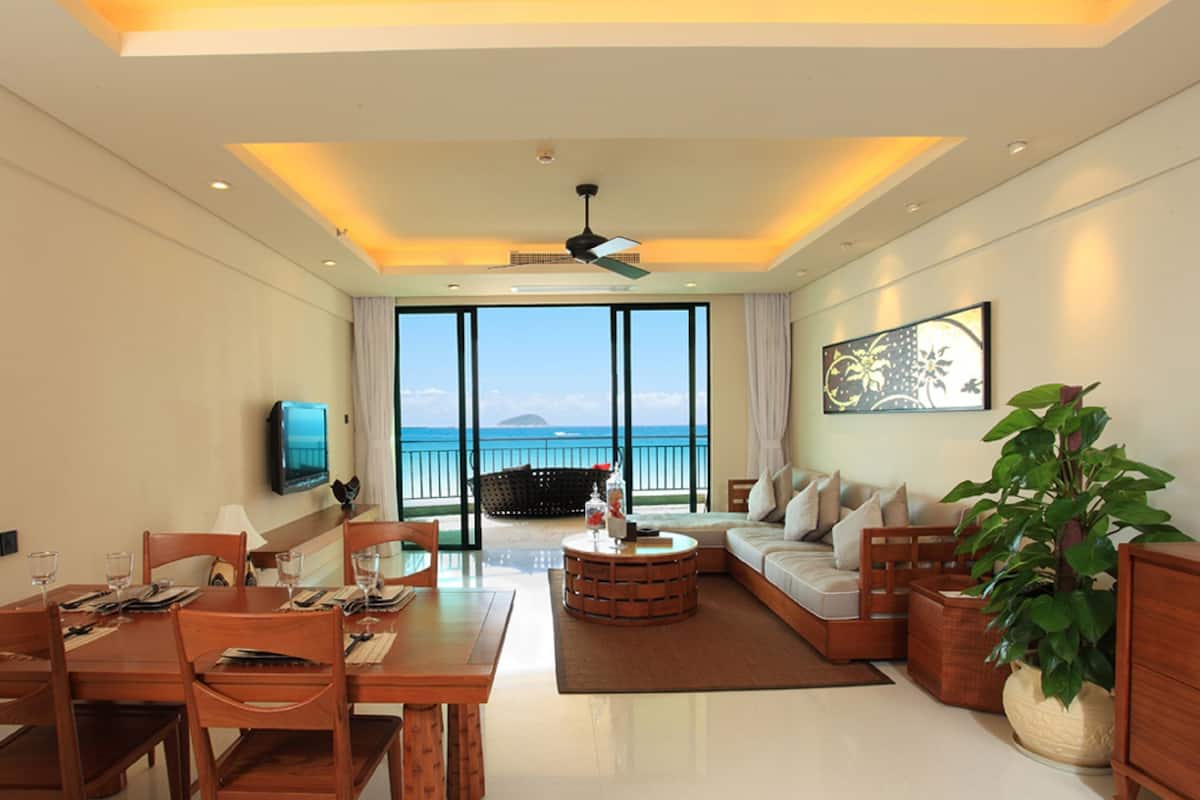 Habitación de hotel moderna con comedor, sofá, mesa de centro y un amplio ventanal con vistas al mar.