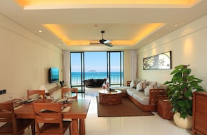 A modern hotel room with a dining area, a sofa, a coffee table, and a large window offering a view of the sea. - Ocean Sonic Resort Sanya (Sanya)