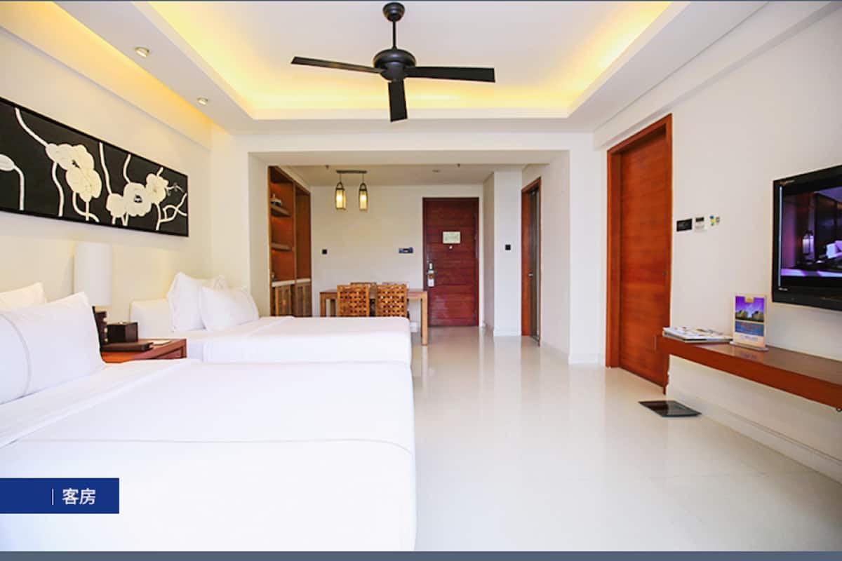 Habitación de hotel con dos camas, un ventilador de techo, un televisor y un cuadro en la pared.