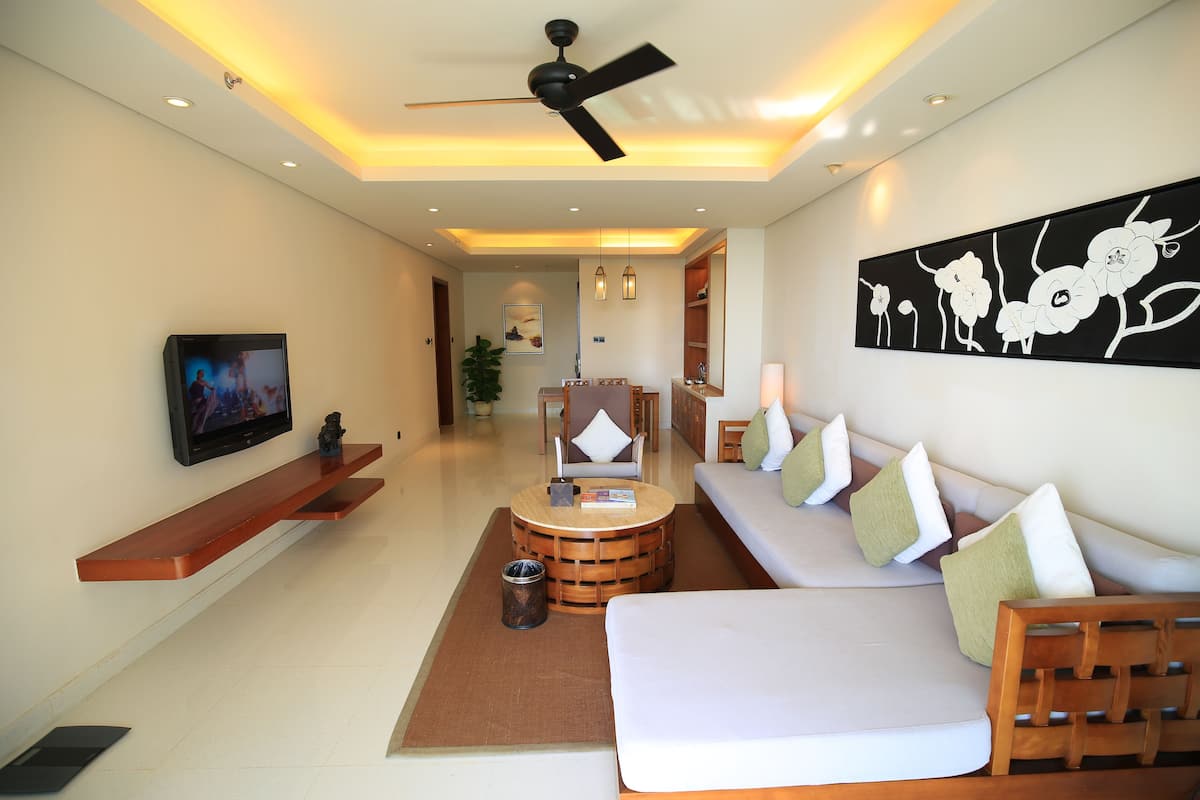 Una habitación de hotel moderna con sofá, televisor, ventilador de techo y una obra de arte en la pared.