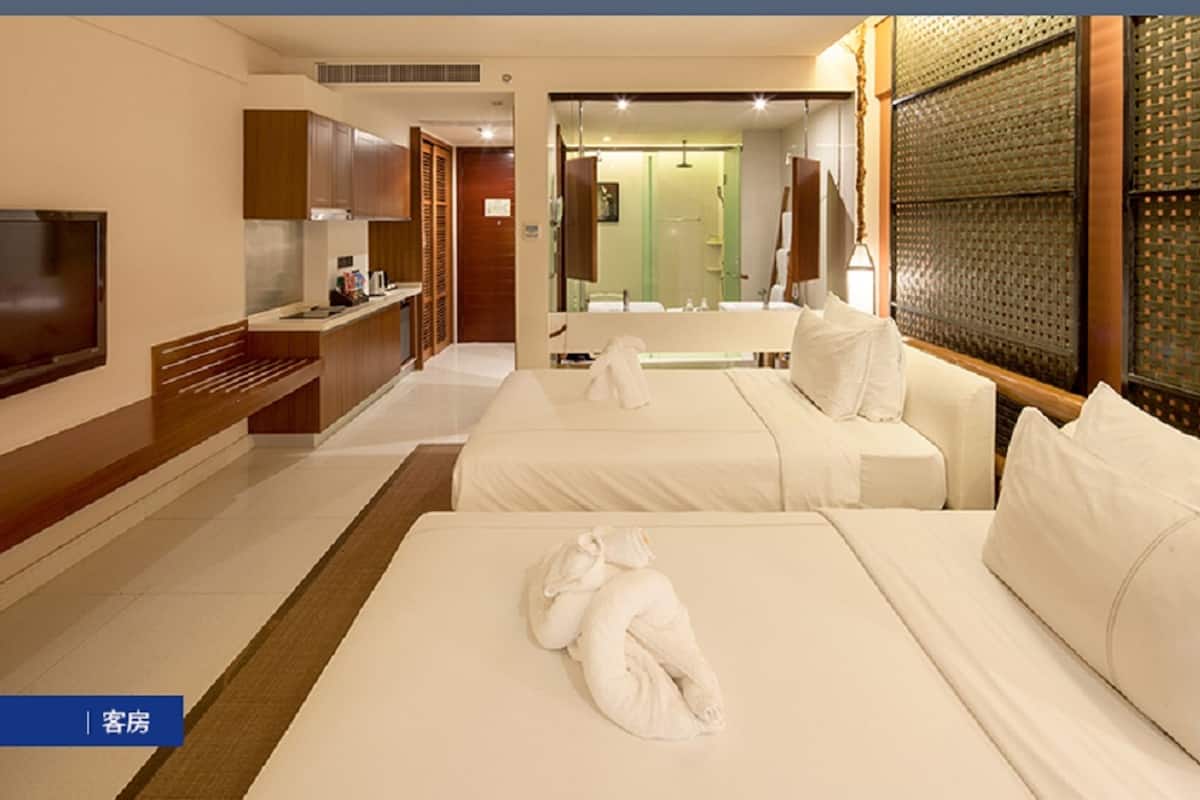 Habitación de hotel con dos camas, televisión, escritorio y baño visible a través de una puerta abierta.
