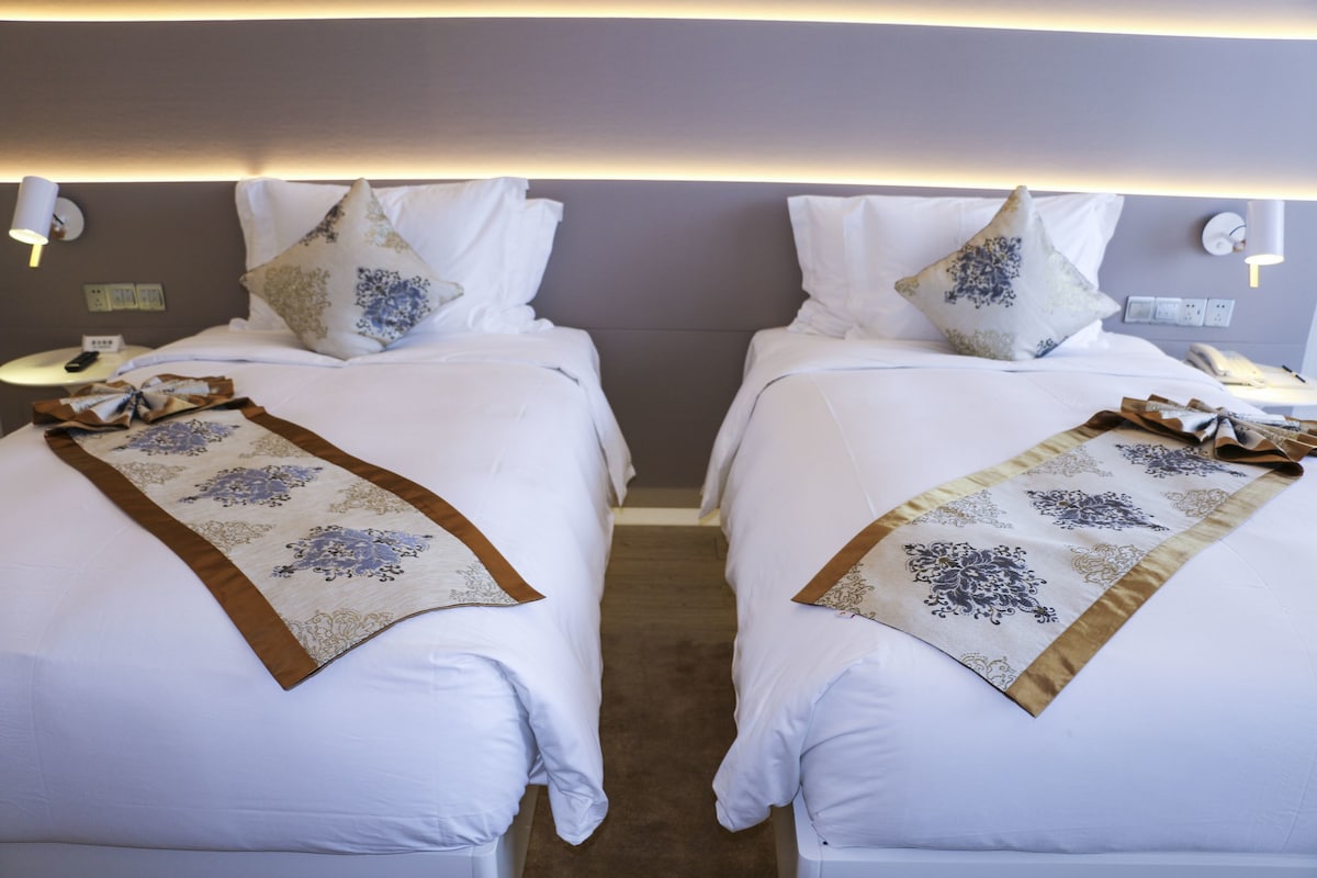 Une chambre d’hôtel avec deux lits, chacun agrémenté d’une couvre-lit à motifs et de coussins, une table de chevet avec une lampe et un téléphone fixé au mur.