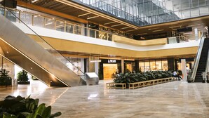Un centro comercial de varios niveles con escaleras mecánicas, una zona de descanso con plantas y una tienda con un letrero en un idioma extranjero.