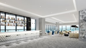 Zona de bar moderna con una barra larga y taburetes, un espacio de estar con sofás y sillones, y un amplio ventanal con vistas.