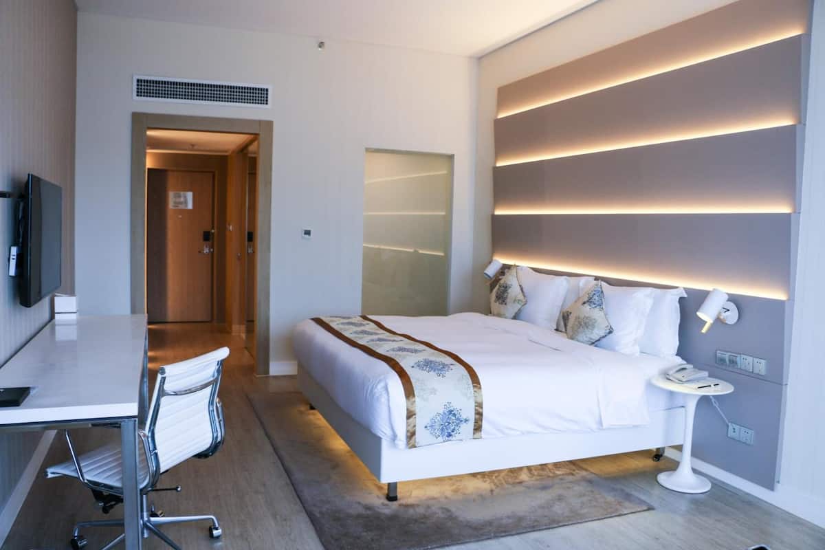 A modern hotel room with a bed, bedside table, desk, and chair.