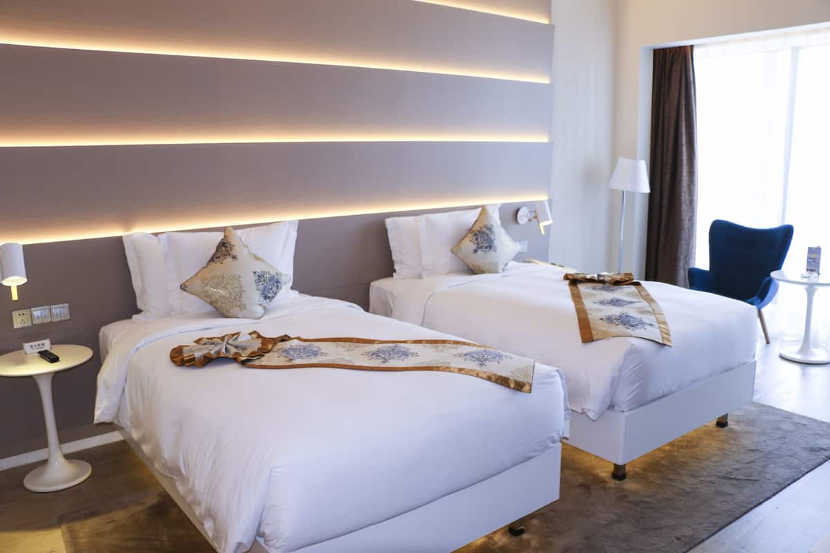 A hotel room with two beds, a small round table, a chair, and a lamp.