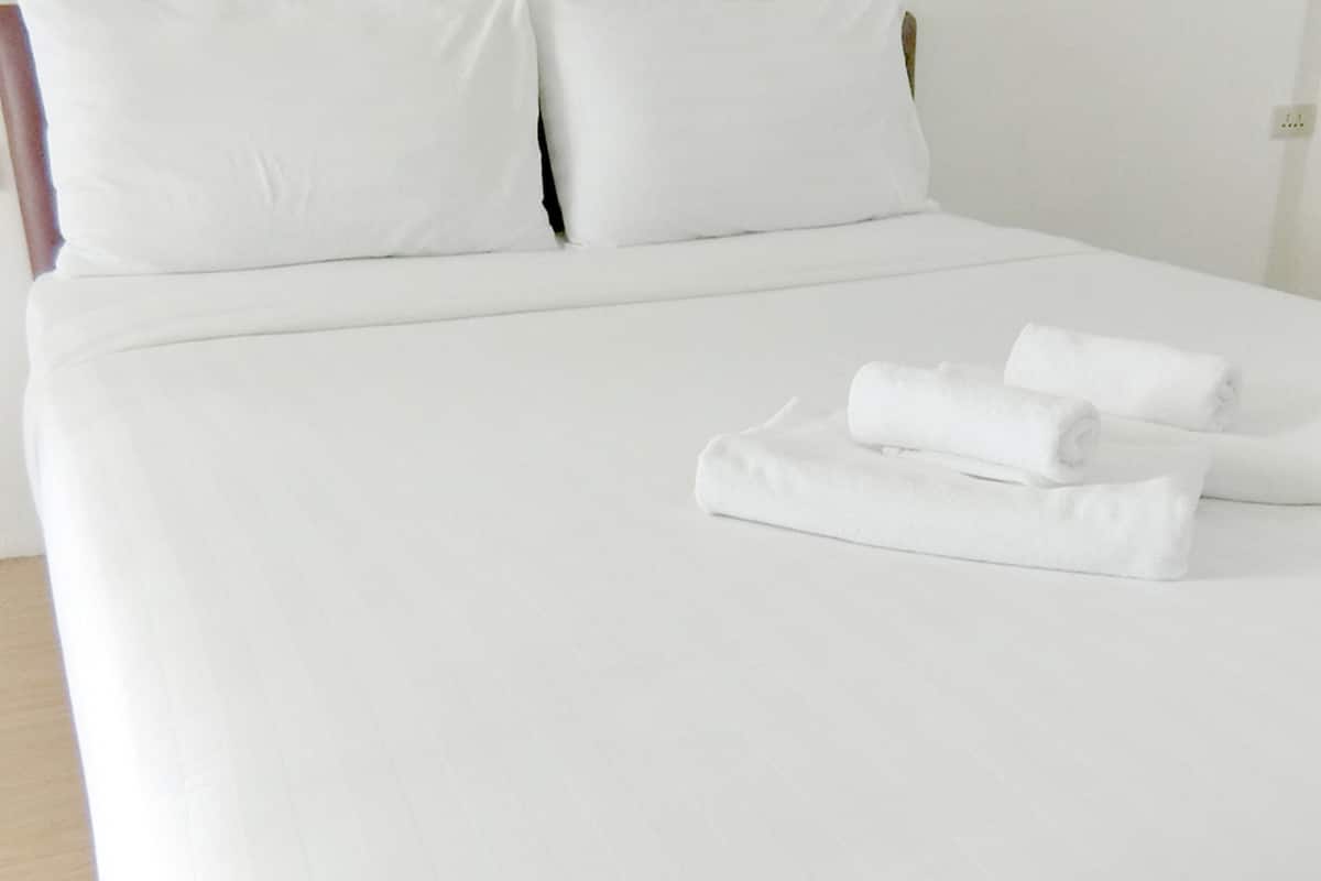 A neatly made bed with white linens and pillows, and two rolled towels placed on the bed.