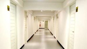 A long, narrow hotel corridor with white walls and doors on both sides. - The Kiri Resitel (Phetchaburi)