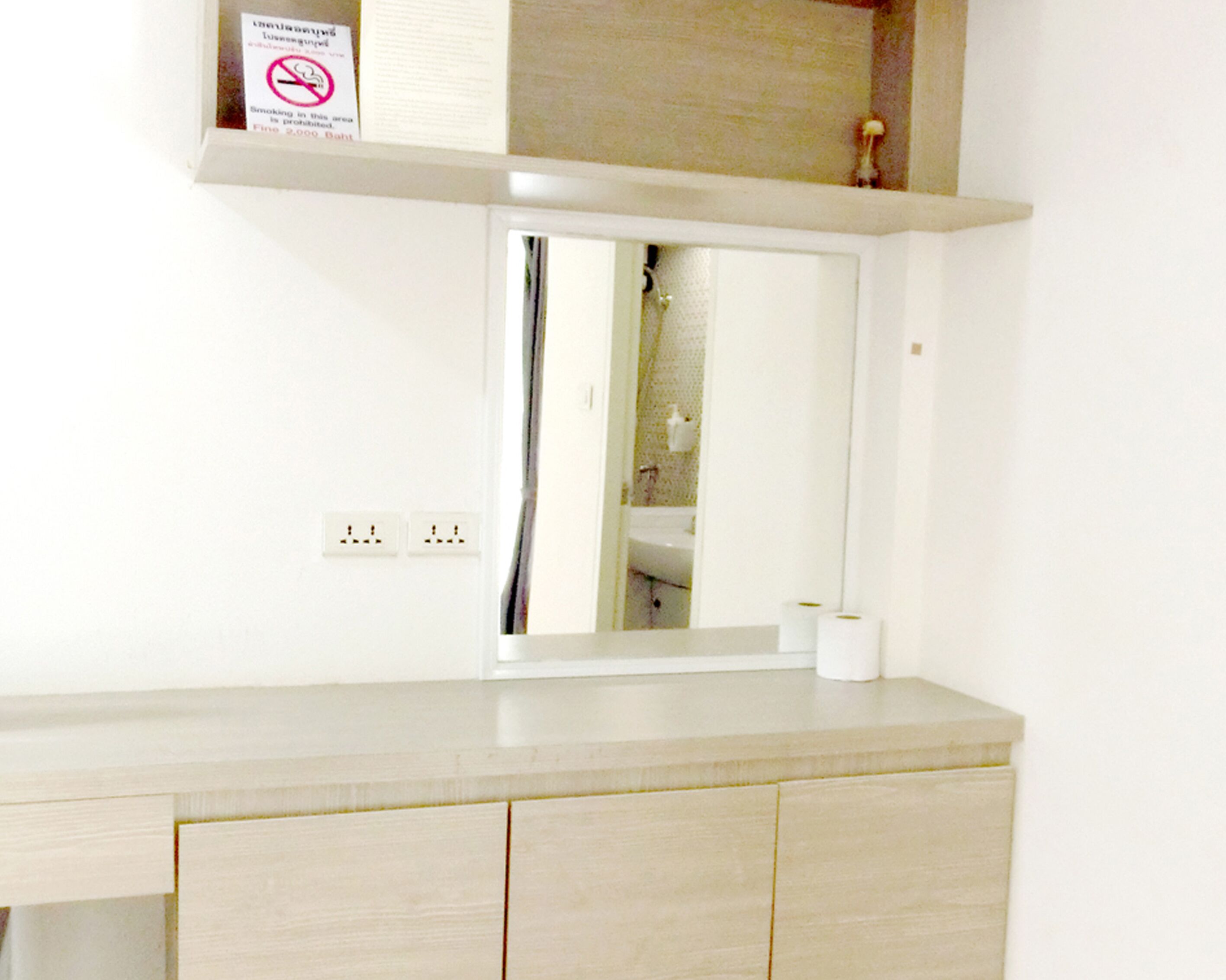 A bathroom with a mirror, a sink, and a toilet. There is a sign prohibiting smoking above the mirror.