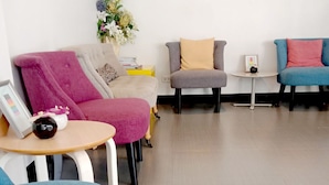 A modern living room with a grey sofa, a pink armchair, and a blue armchair. There is a small table with a picture frame and a decorative item. - The Kiri Resitel (Phetchaburi)