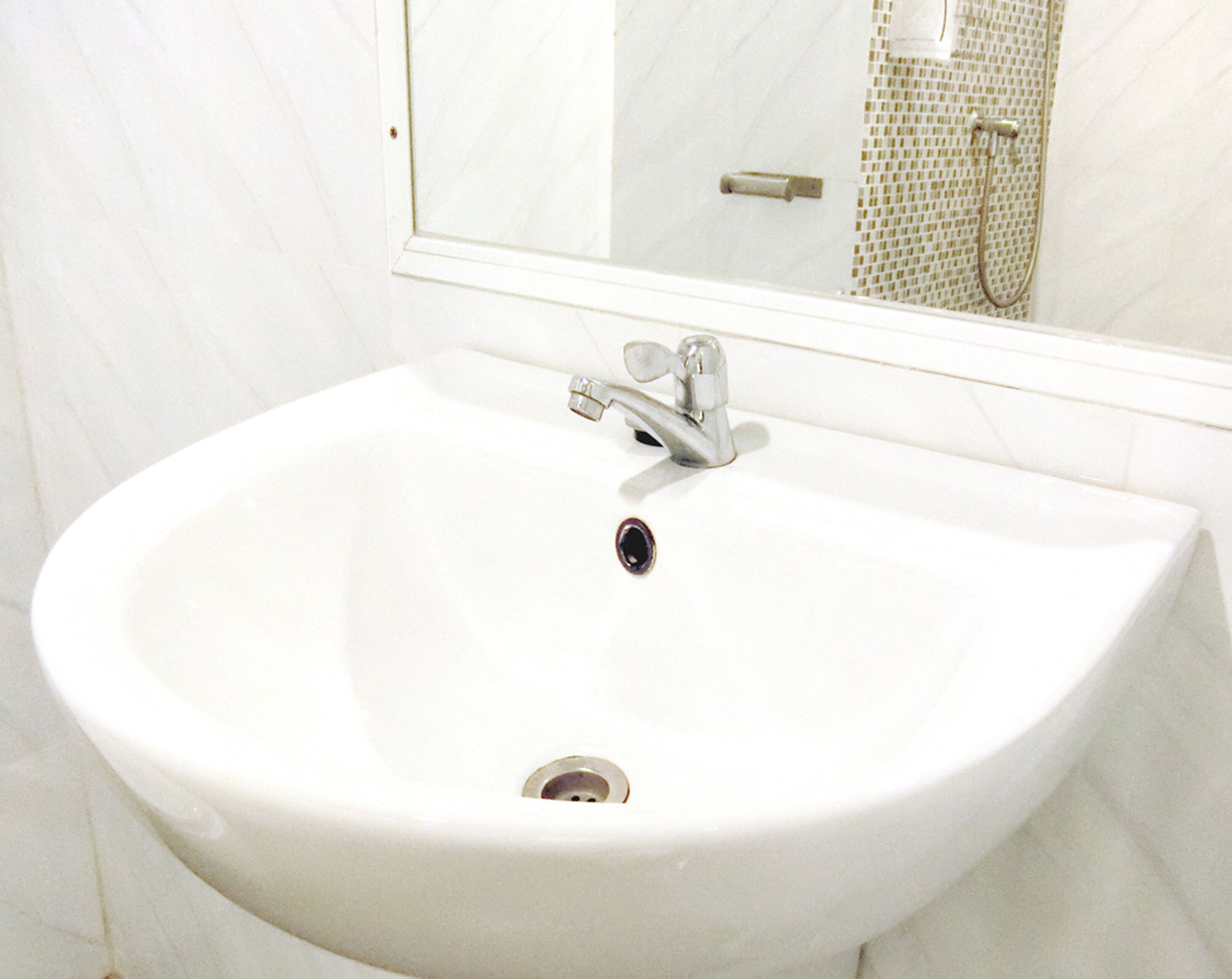Ein weißes Waschbecken mit einem Wasserhahn, ein Spiegel darüber und eine geflieste Wand.
