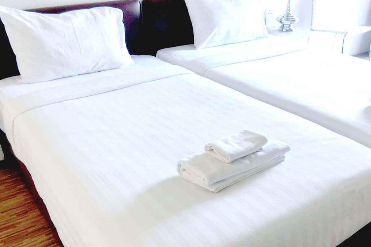 A hotel room with two beds, each with white linens and pillows. There are folded towels on the beds.