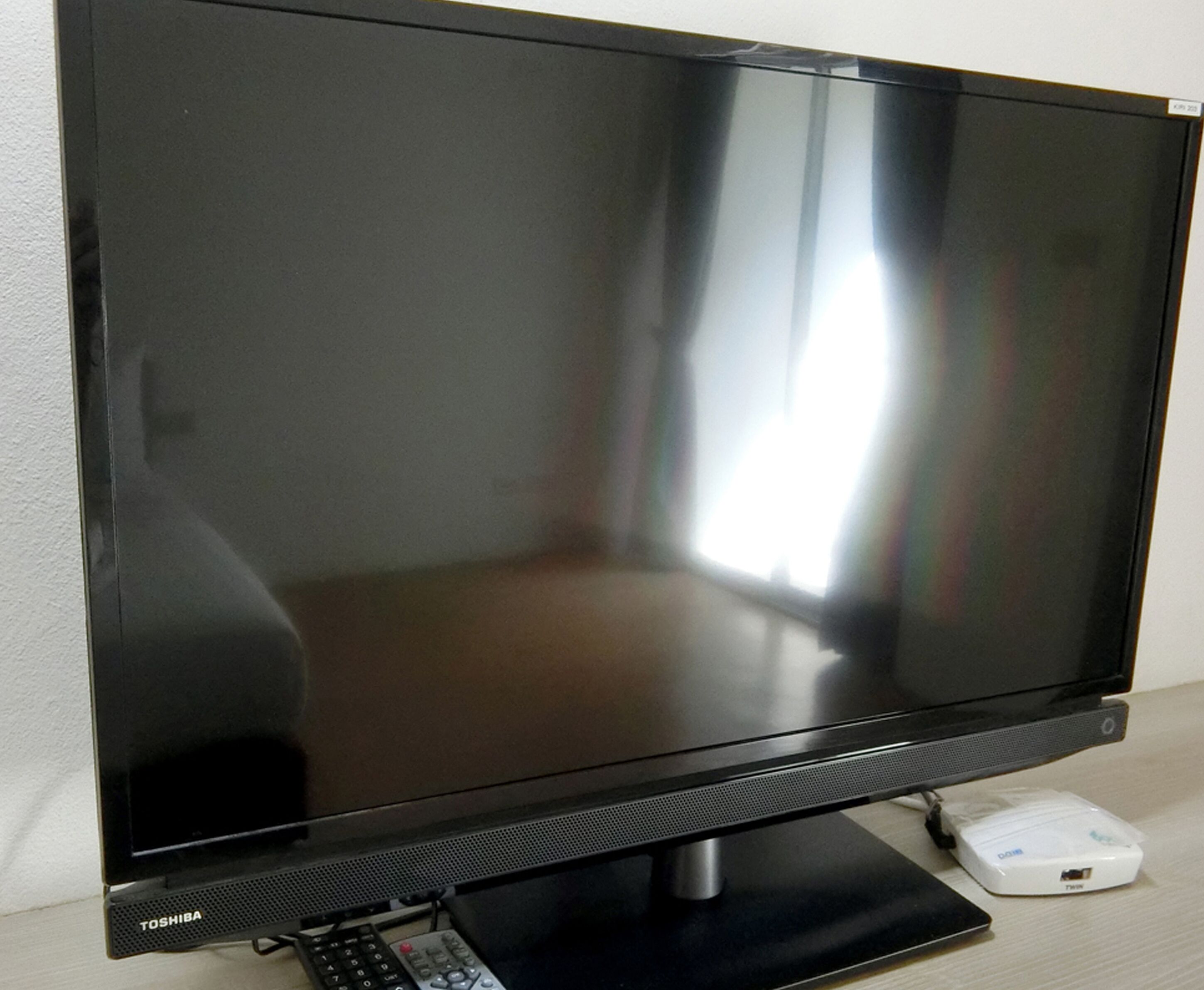 A flat-screen TV with a stand and remote control, placed on a wooden surface.