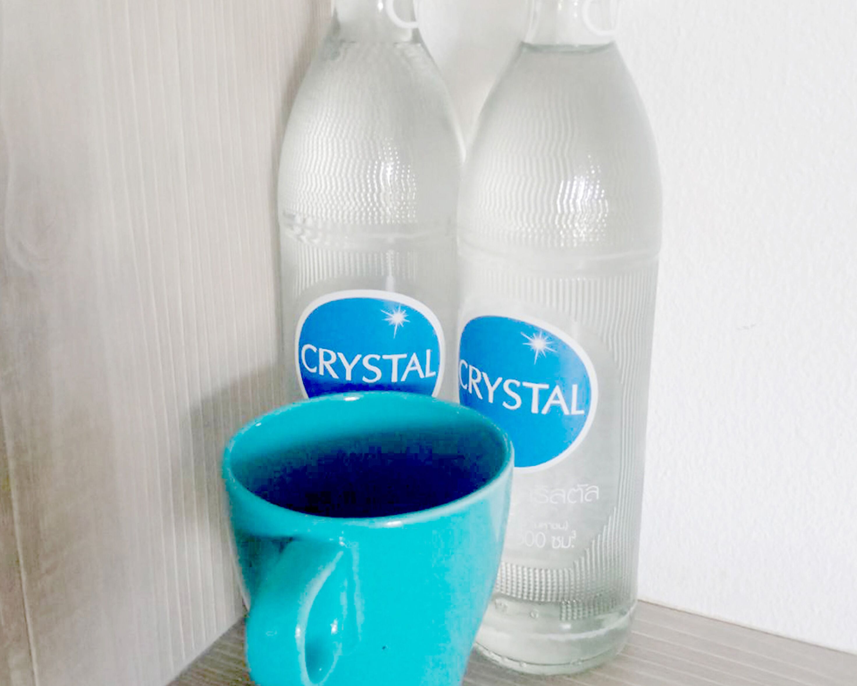Two bottles labeled 'CRYSTAL' and a turquoise mug on a shelf.