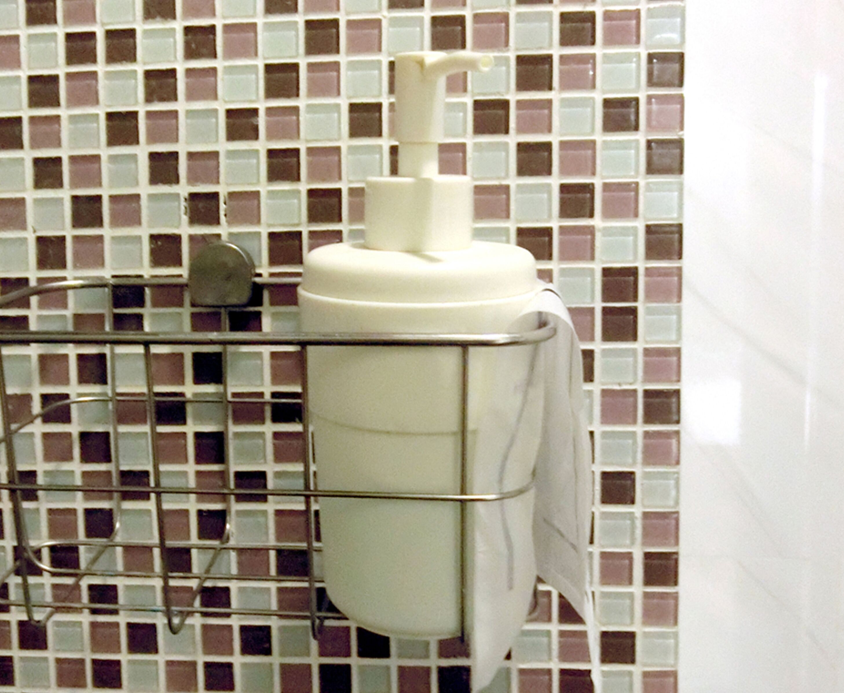 A hand sanitizer dispenser mounted on a metal rack against a tiled wall.