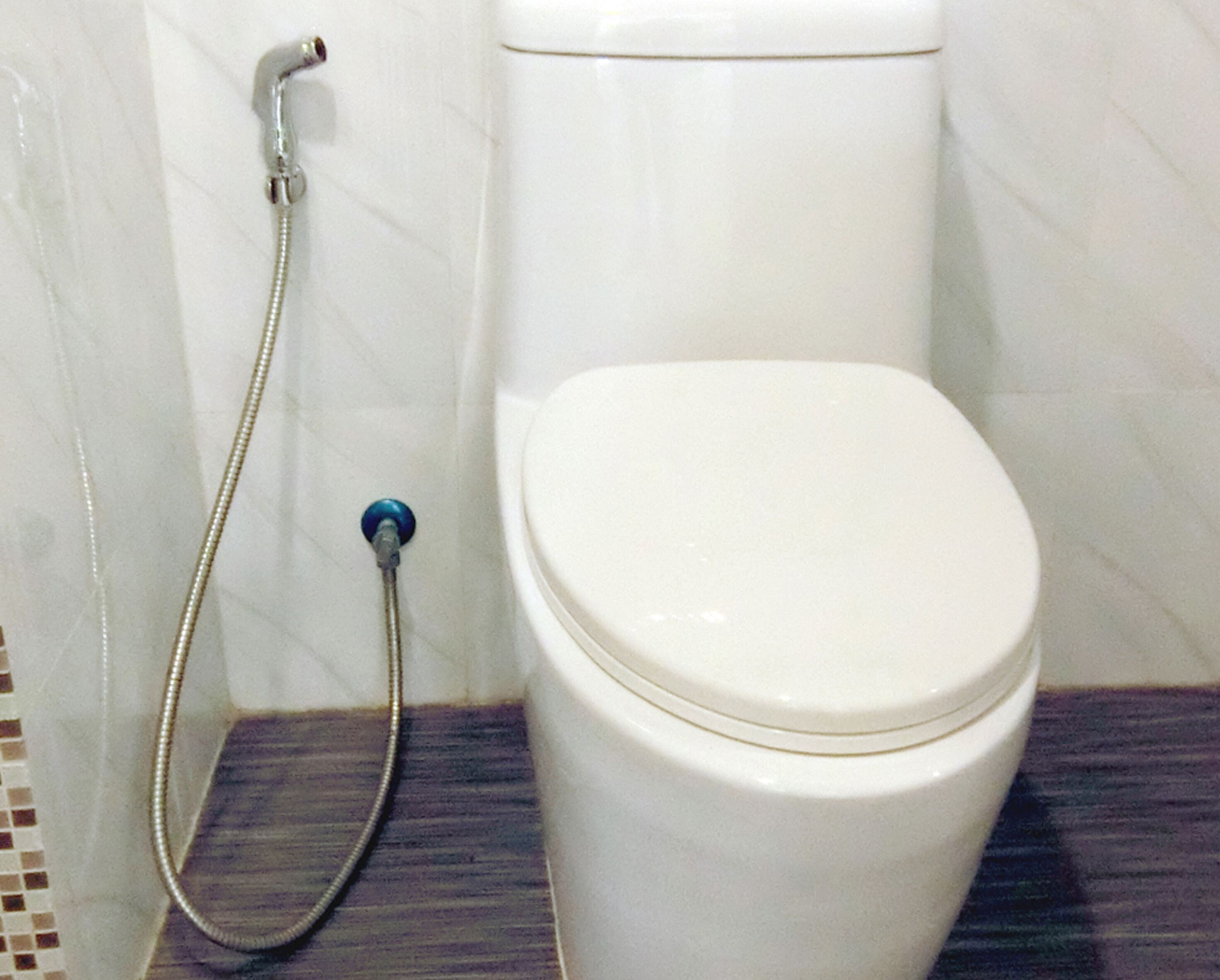 A white toilet with a closed lid, a shower head attached to the wall, and a tiled floor.