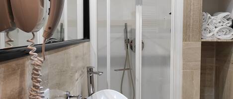 Un baño moderno con ducha de vidrio, lavamanos blanco y un secador de pelo en la encimera.