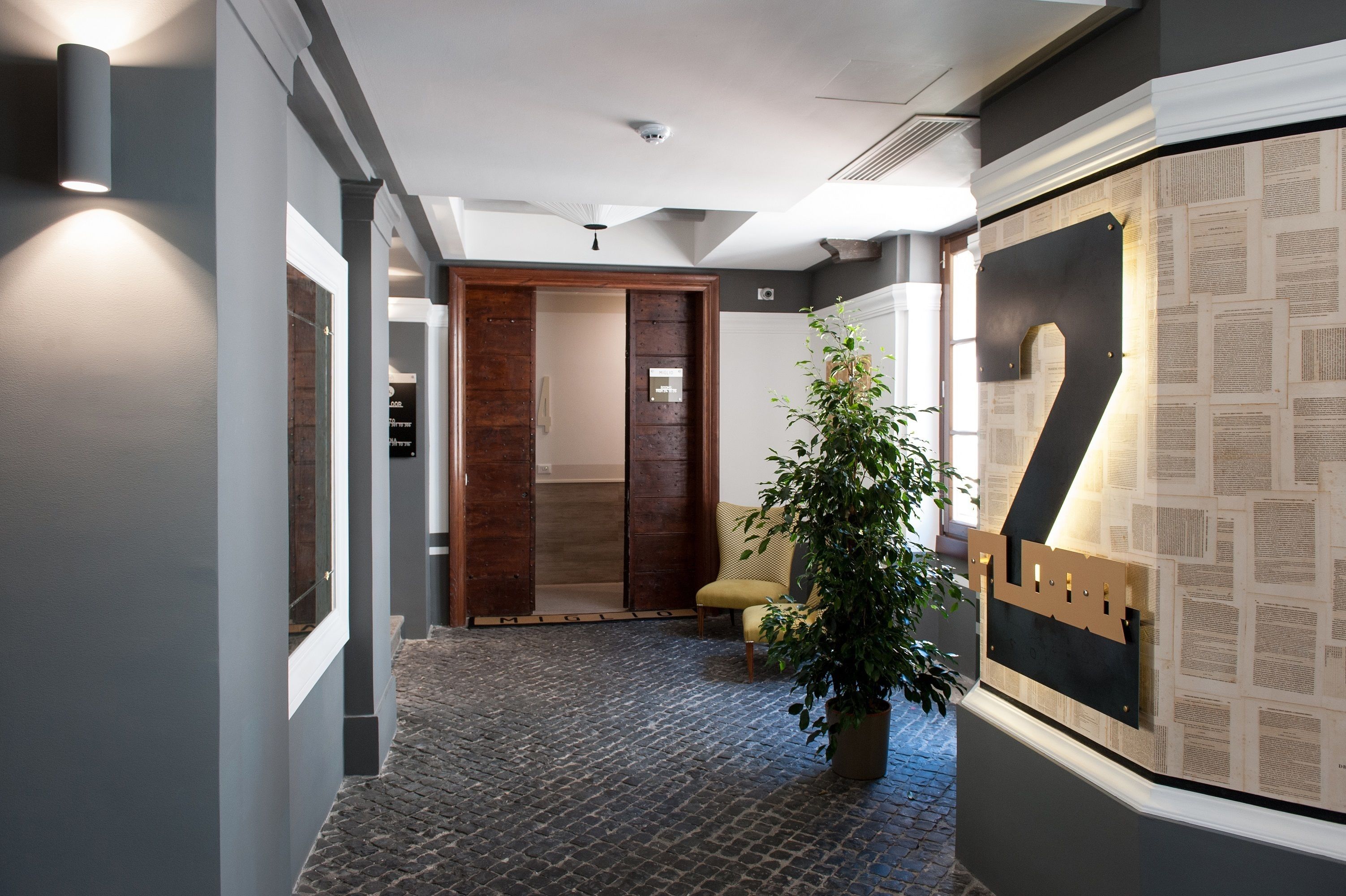 Un couloir avec une porte en bois, une plante en pot et un mur orné d’un grand chiffre « 2 ».