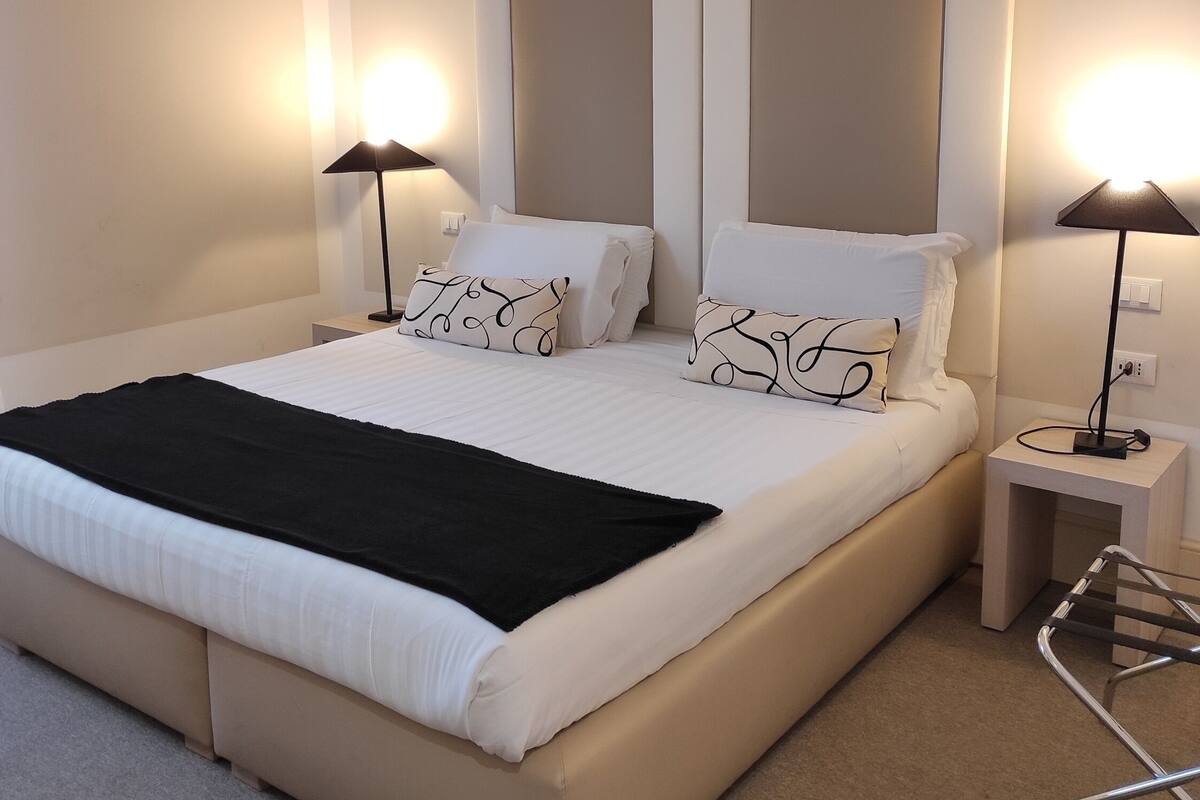 Una moderna camera d'albergo con un letto grande, due comodini e una poltrona.