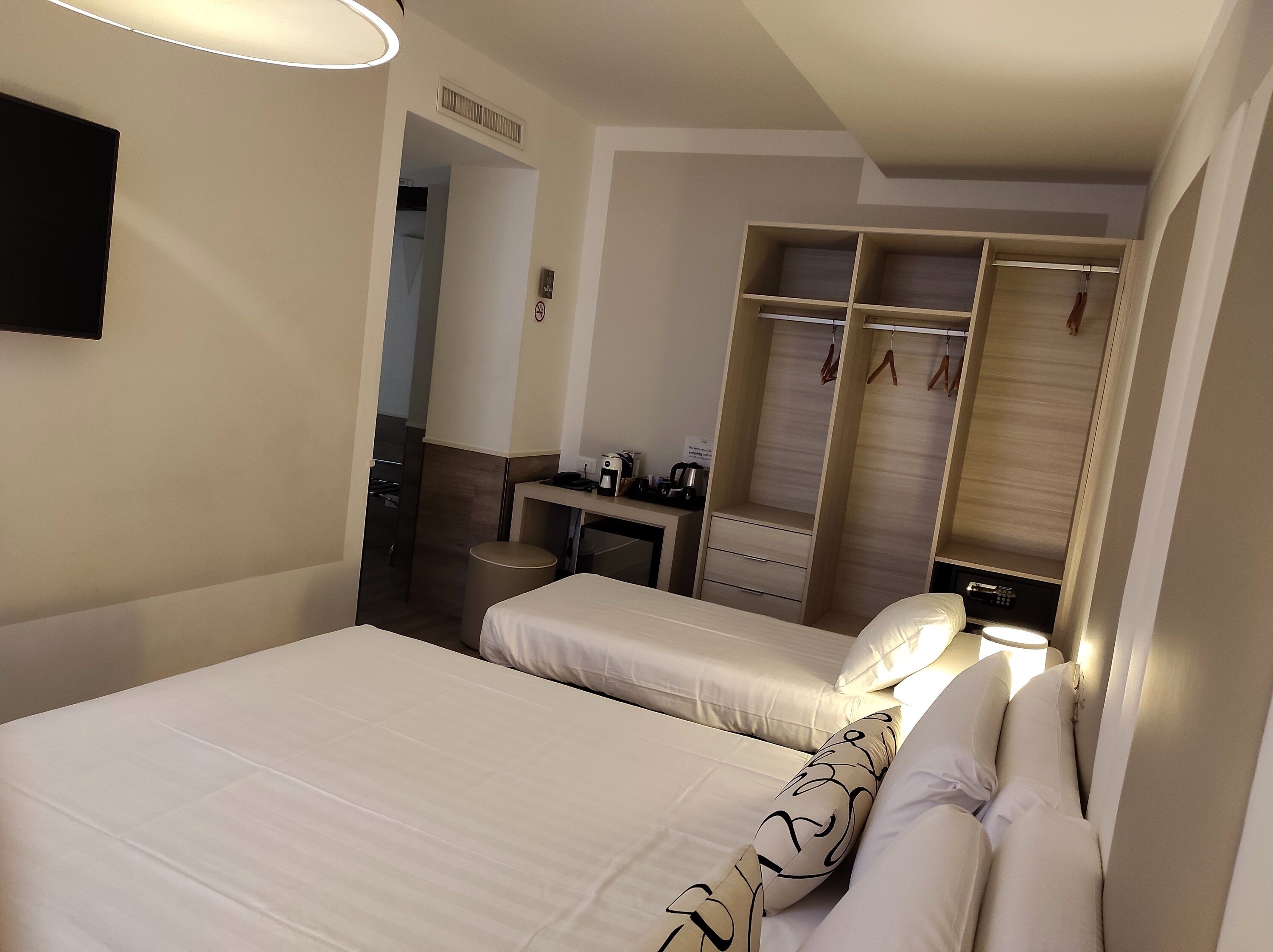 Una habitación de hotel con cama, mesita de noche y vestidor con espacio para colgar ropa.