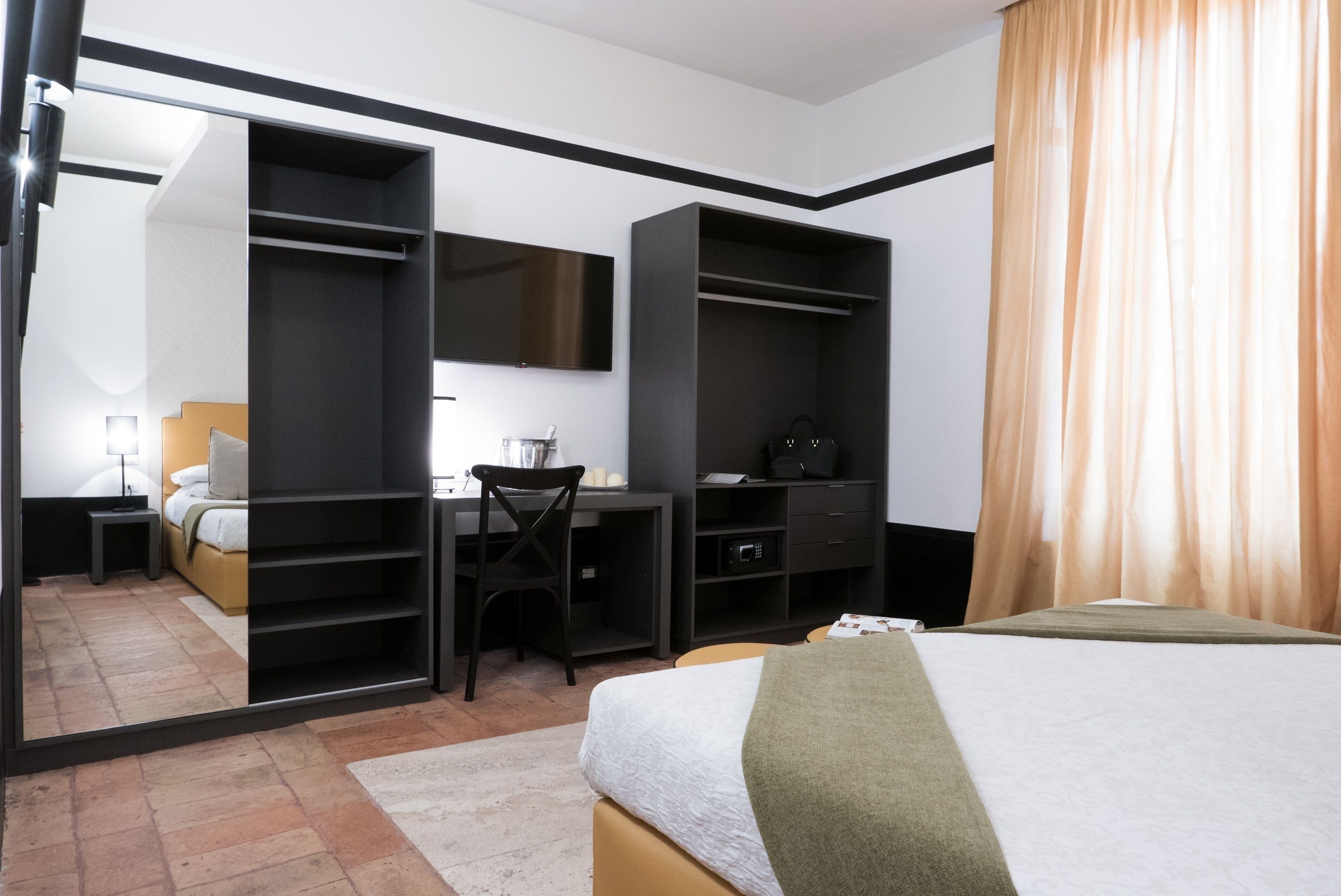 A hotel room with a bed, a desk, a chair, a wardrobe, and a television.