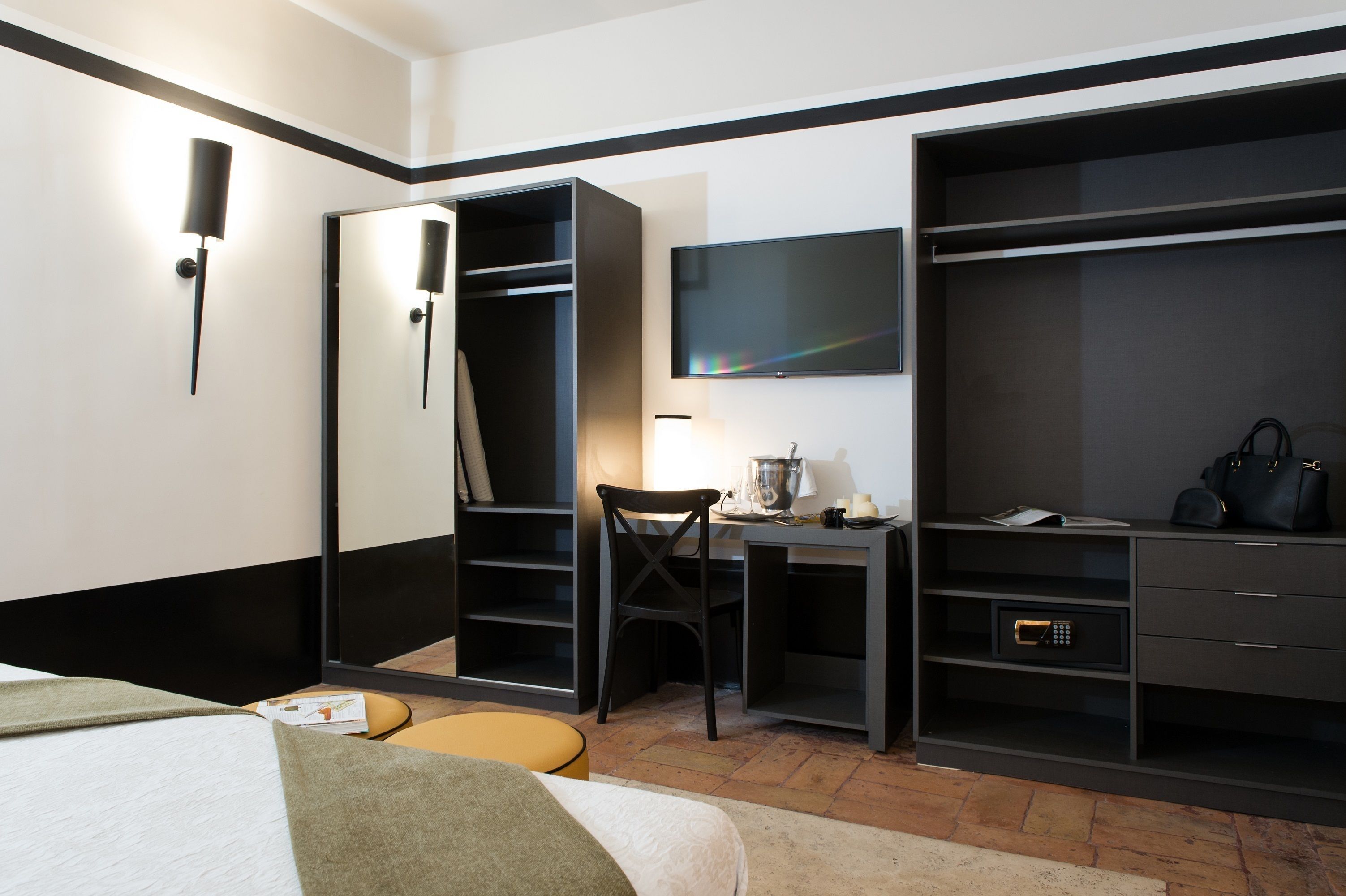 Habitación de hotel con cama, escritorio con silla, televisor, armario y caja fuerte.