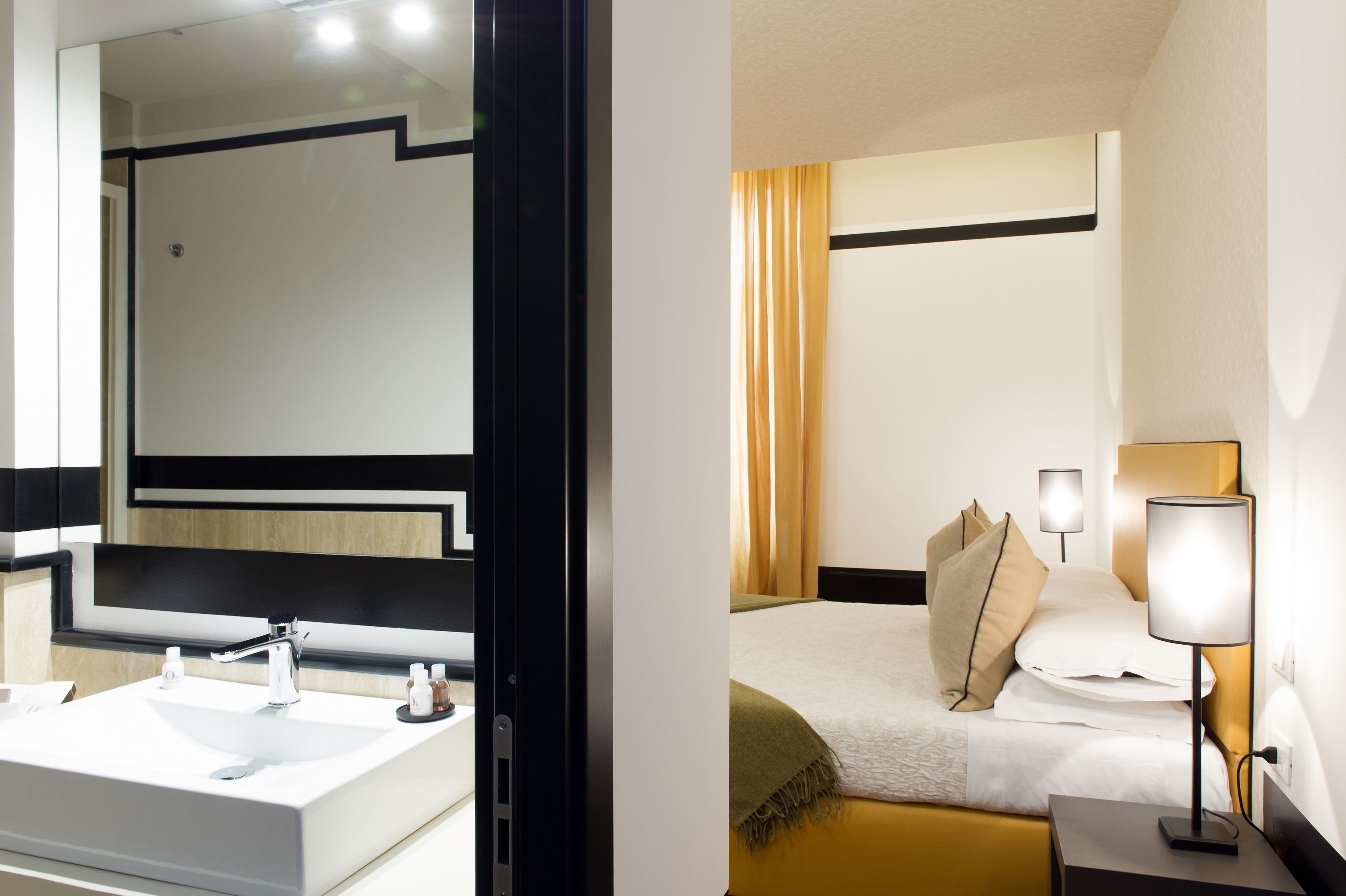 A modern bathroom with a large mirror, white sink, and black-framed mirror. The room has a clean, minimalist design with a beige wall and a black accent strip.