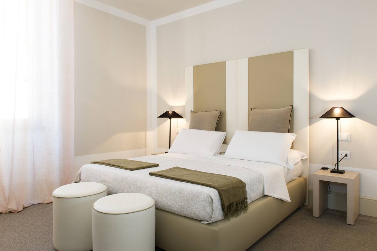 Una camera d'albergo moderna con un letto grande, due comodini e una finestra con tende.