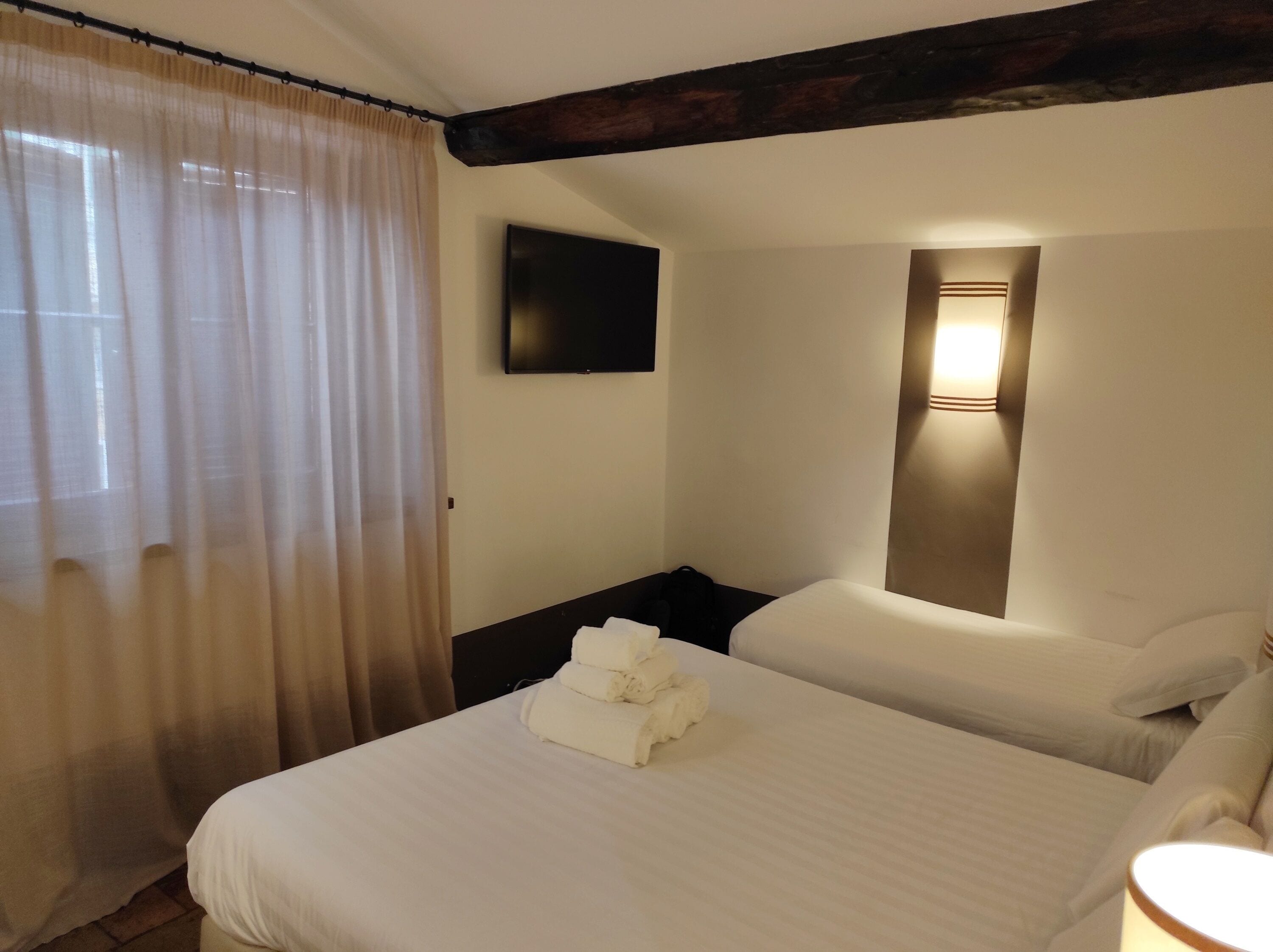 A hotel room with a bed, a TV mounted on the wall, and a bedside lamp.