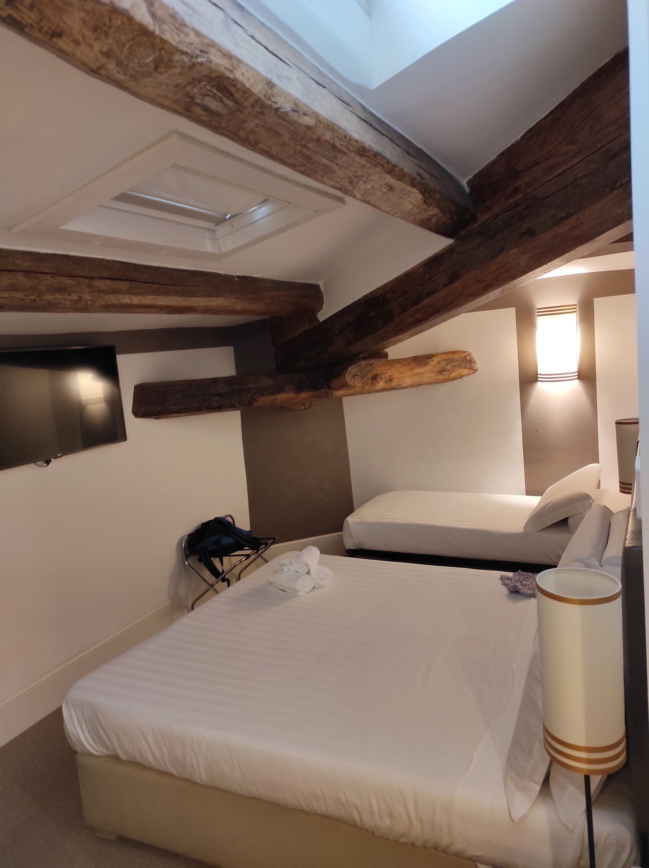 A bedroom with a bed, a chair, a lamp, and a wall-mounted TV.