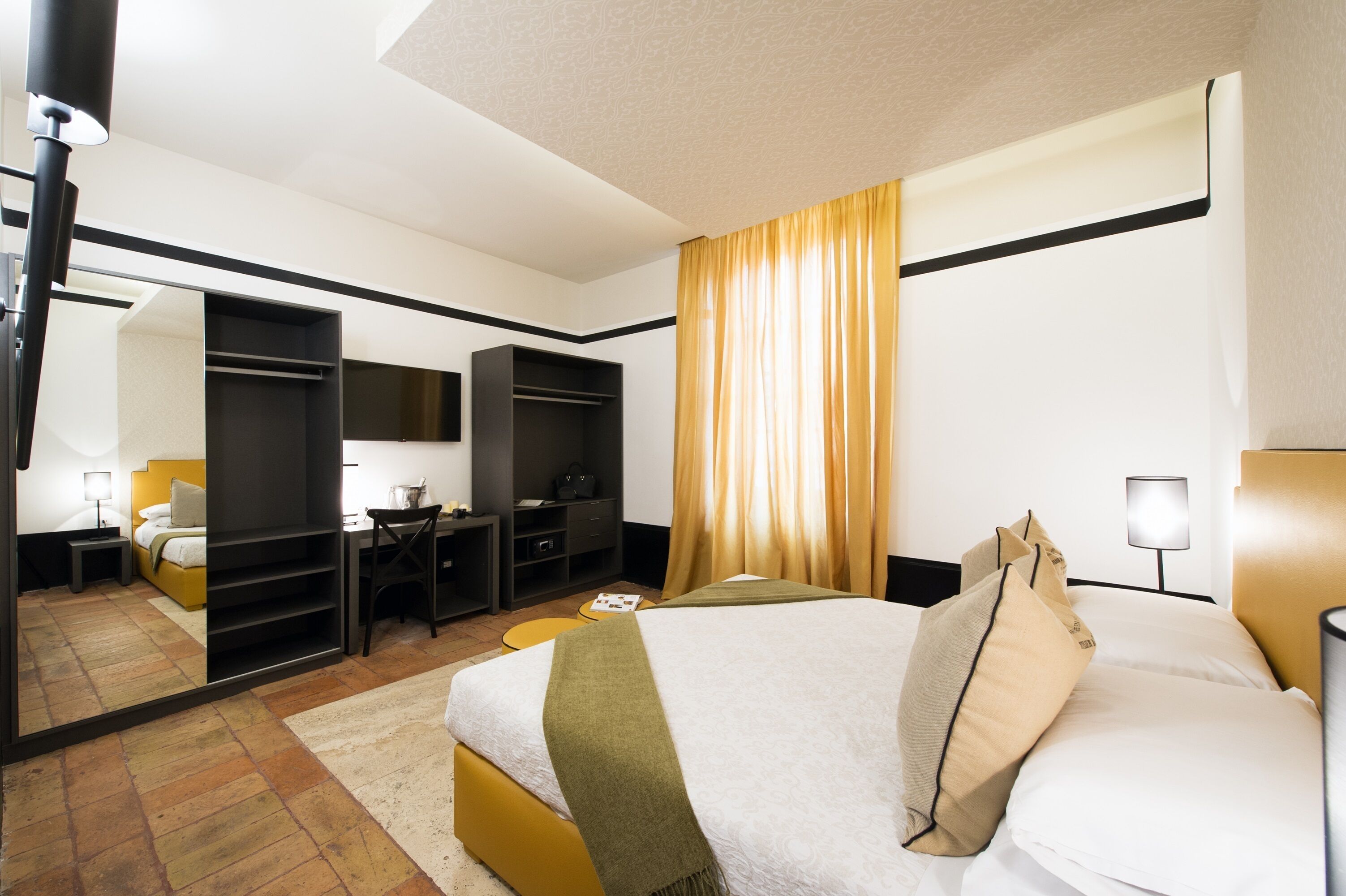 A hotel room with a bed, a desk, a wardrobe, and a mirror.