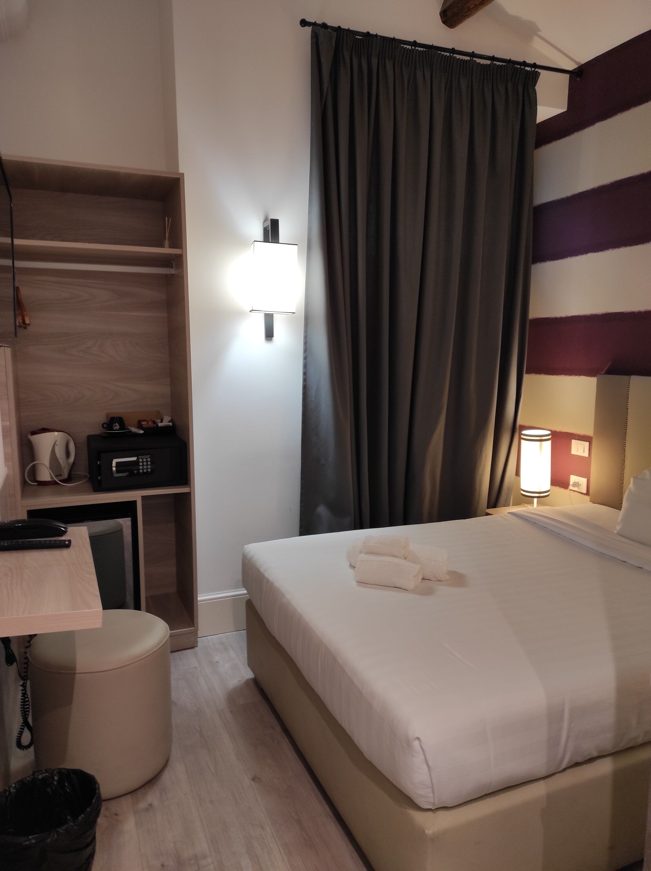 Quarto de hotel com cama, mesa de cabeceira, abajur e guarda-roupa.