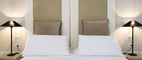 A double bed with white linens, two bedside lamps, and a neutral-toned headboard.