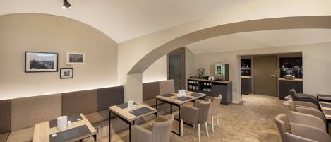 Un café moderno con suelo de patrón hexagonal, mesas de madera con individuales negros y sillas tapizadas en gris.
