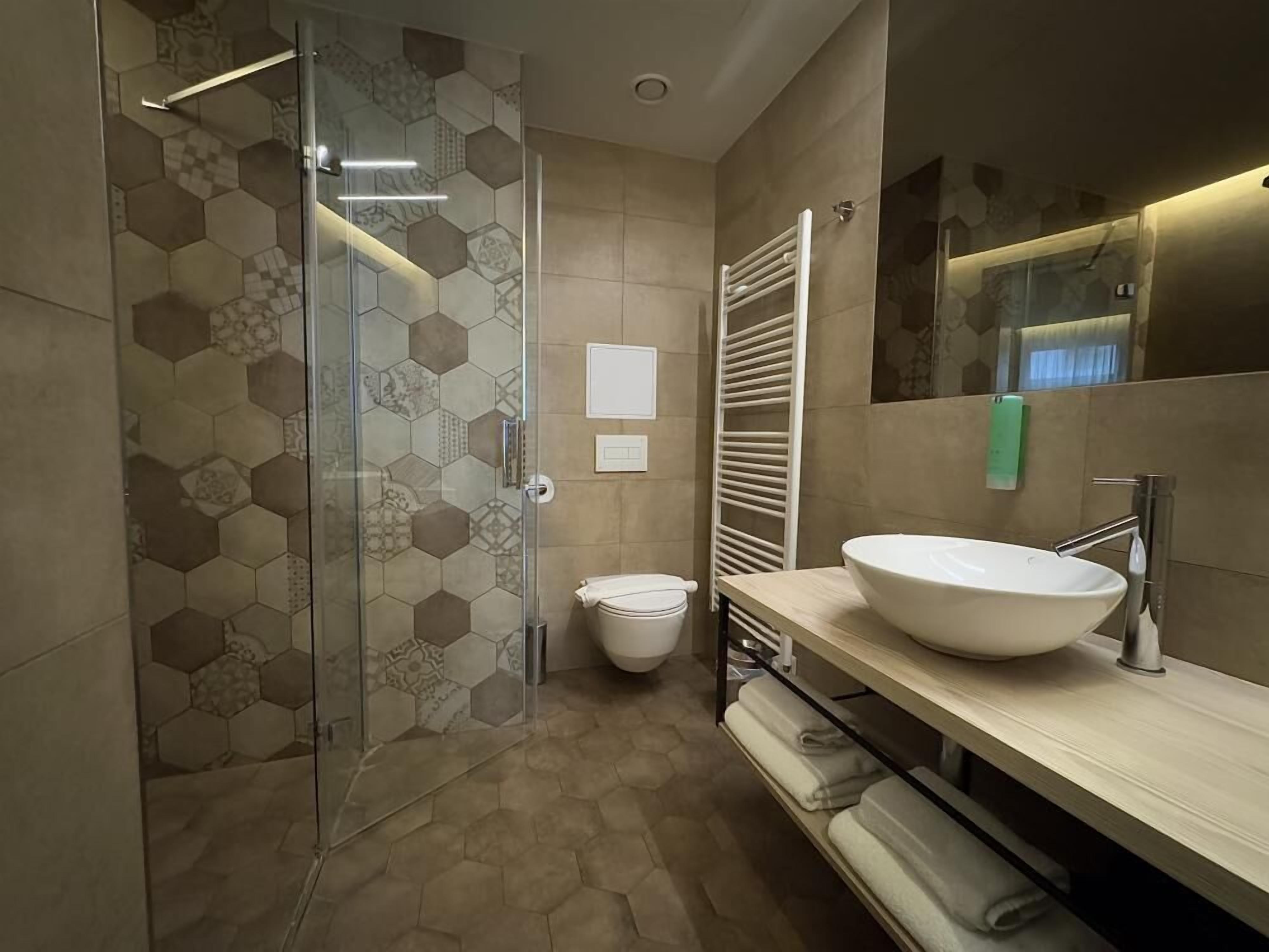 A modern bathroom with a glass shower enclosure, a large white sink, and a towel rack.