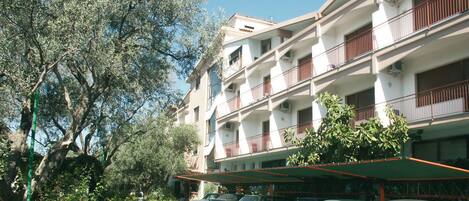 Un edificio de varios pisos con balcones, coches aparcados y un árbol en primer plano.