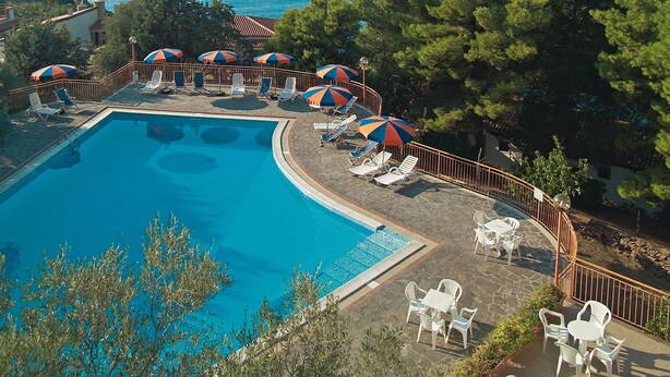 Un espace piscine aménagé avec des chaises longues et des parasols, entouré d’arbres et offrant une vue sur une étendue d’eau.