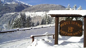 Placa de madeira para um hotel e restaurante com vista para montanhas e árvores cobertas de neve.