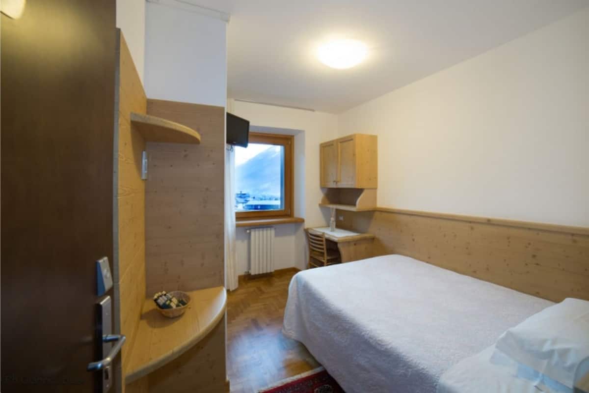Un dormitorio con cama, un armario de madera, una mesita, una ventana con vistas y un radiador.