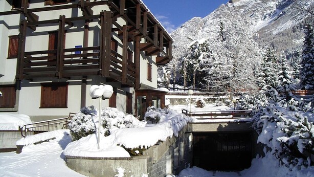 Um chalé com varanda de madeira, rodeado por árvores e montanhas cobertas de neve.