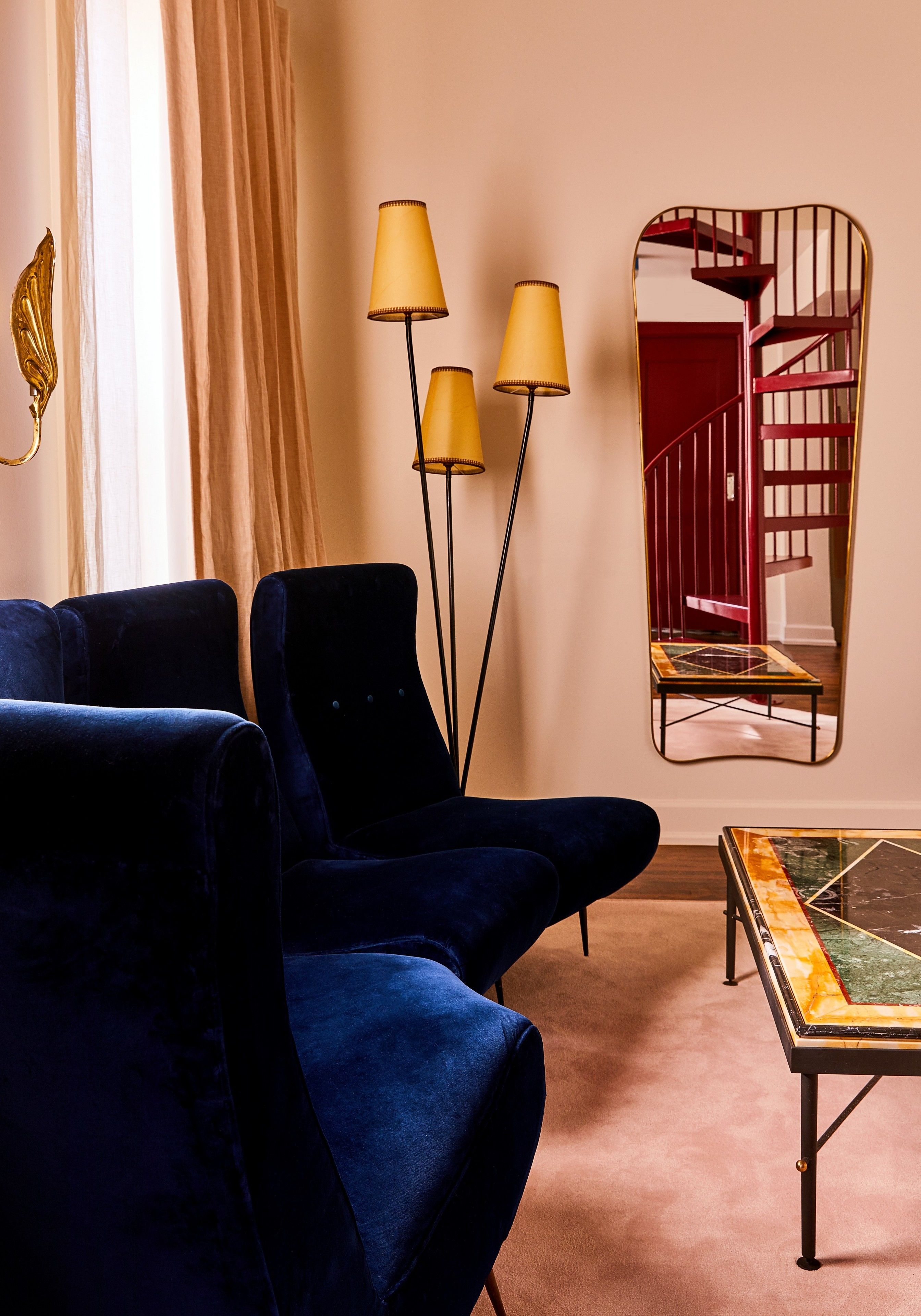 A room with a blue armchair, a floor lamp, a mirror, and a coffee table.