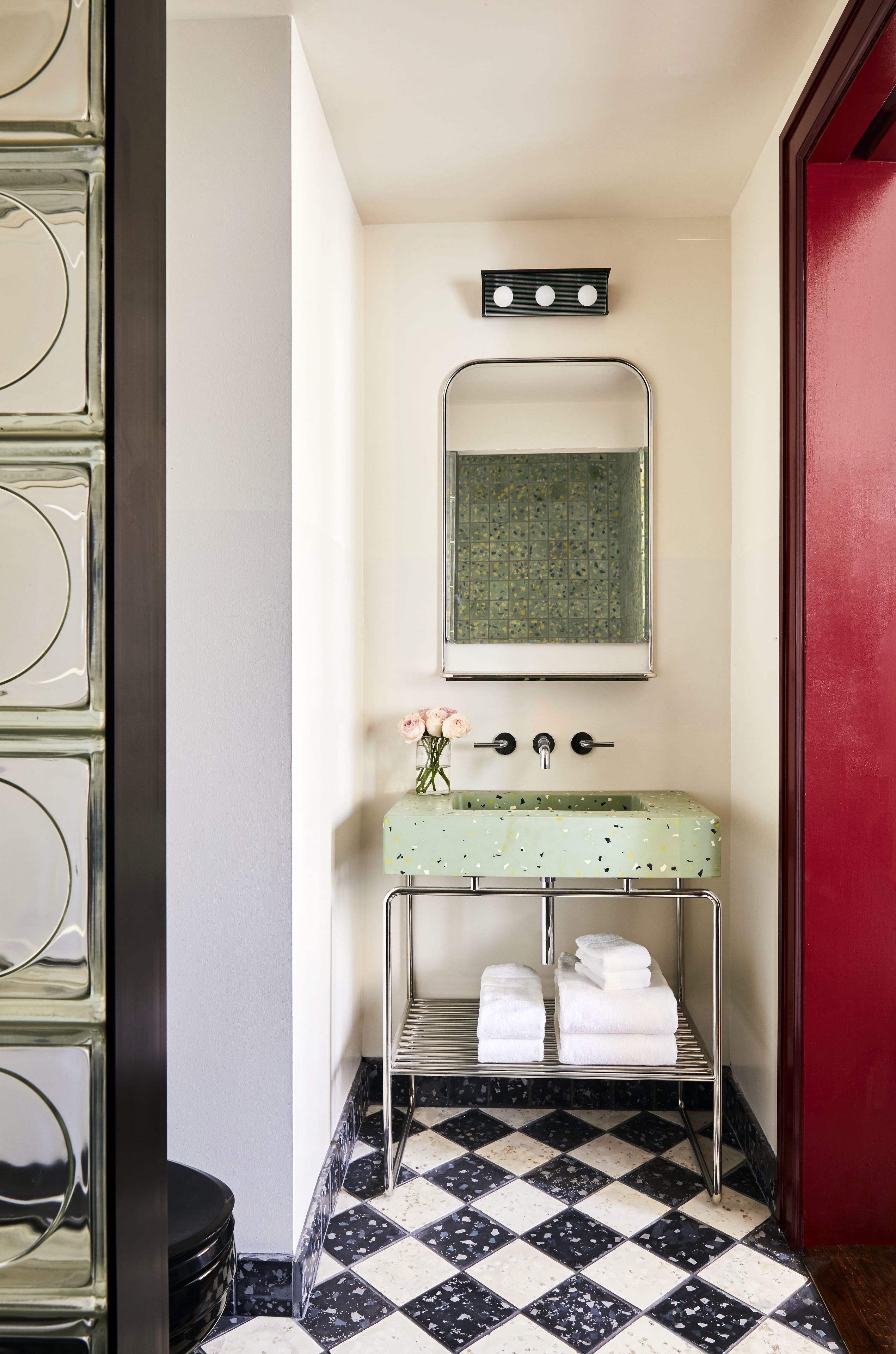 A bathroom with a checkered floor, a green vanity with a mirror, and a red door.