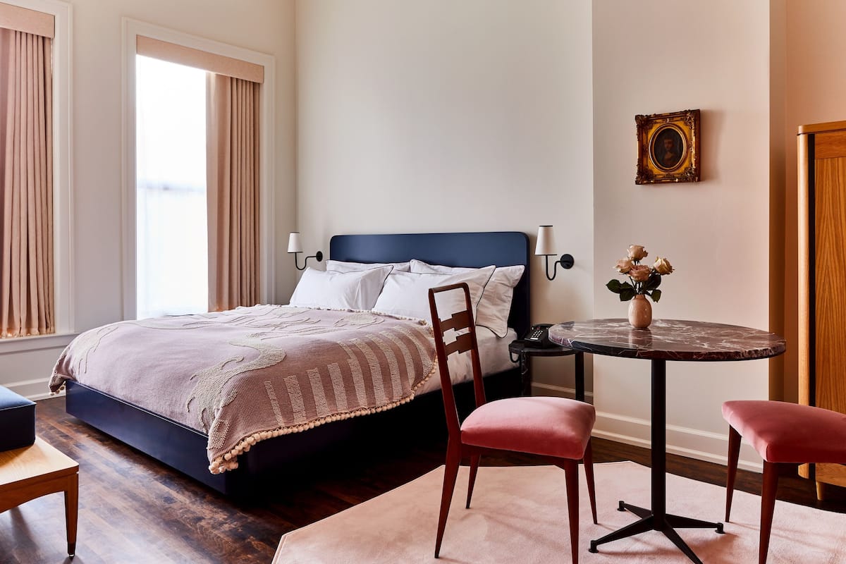 A bedroom with a bed, a chair, a small table, and a picture on the wall.