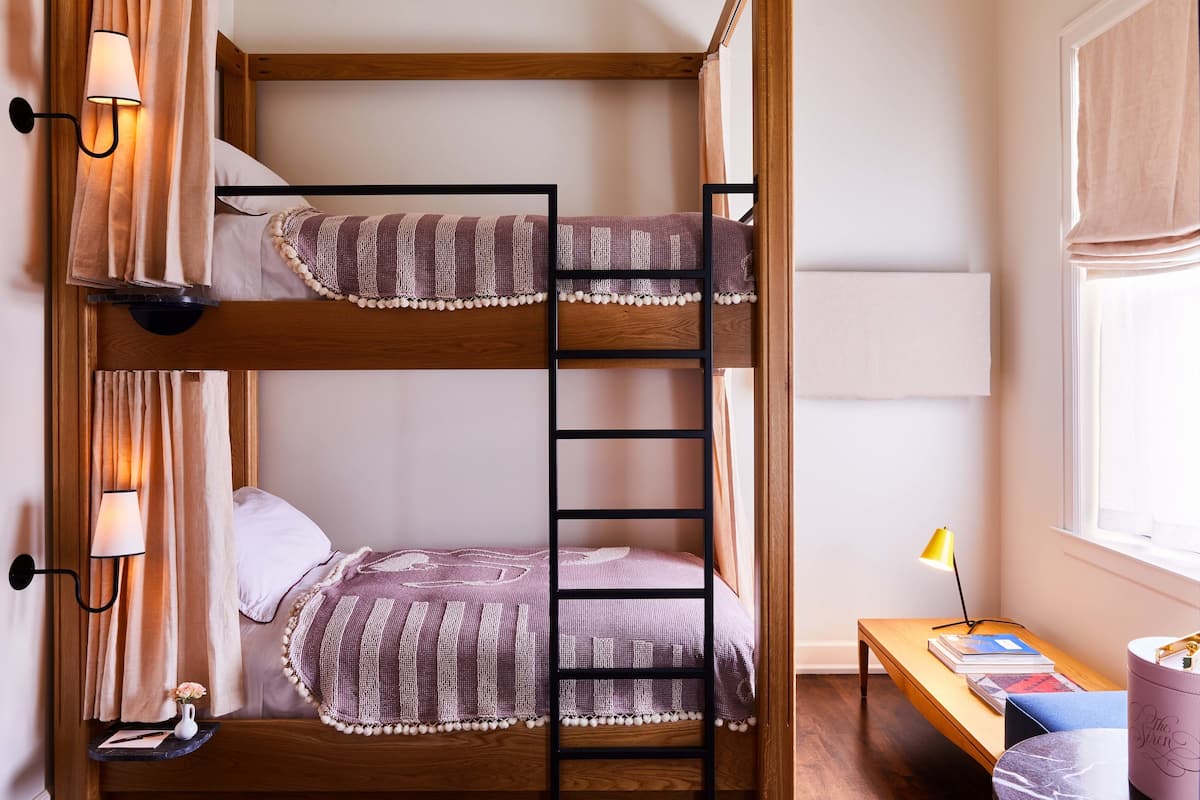 A bunk bed with a ladder, a bedside table with books, and a lamp.