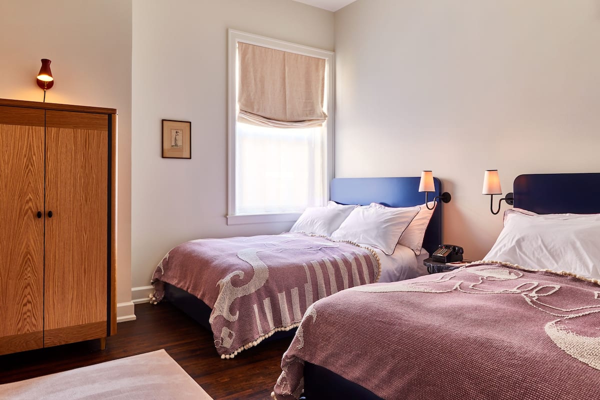 A bedroom with two beds, a wardrobe, a window with a curtain, and bedside lamps.