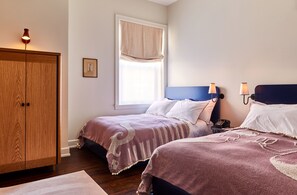 A bedroom with two beds, a wardrobe, a window with a curtain, and bedside lamps.