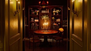 A warmly lit room with a round table, two chairs, a chandelier, and a floral arrangement. - The Siren Hotel, an Ash Hotel (Detroit)
