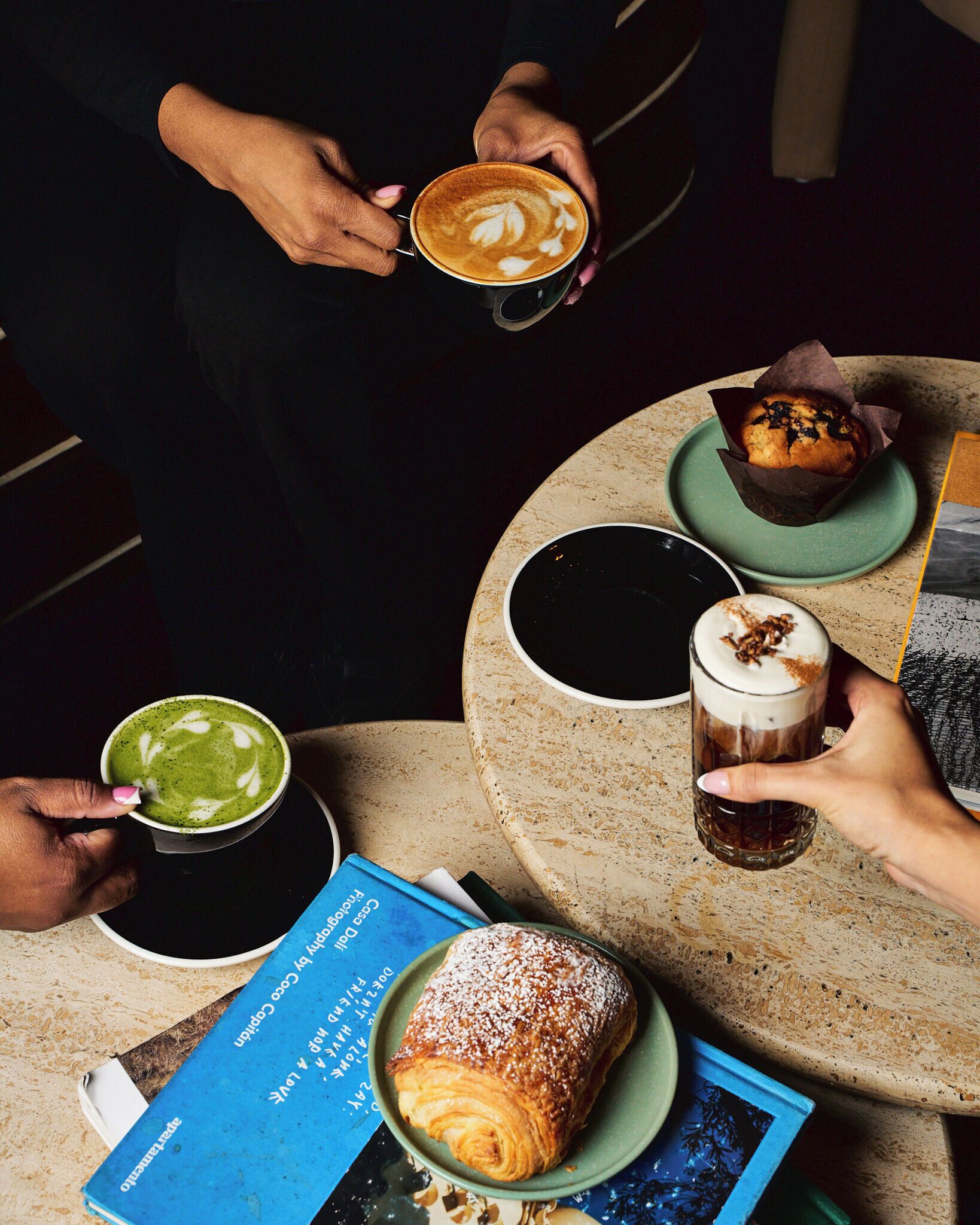 Una mesa con diversas bebidas y pastelería, incluyendo un croissant y un muffin.