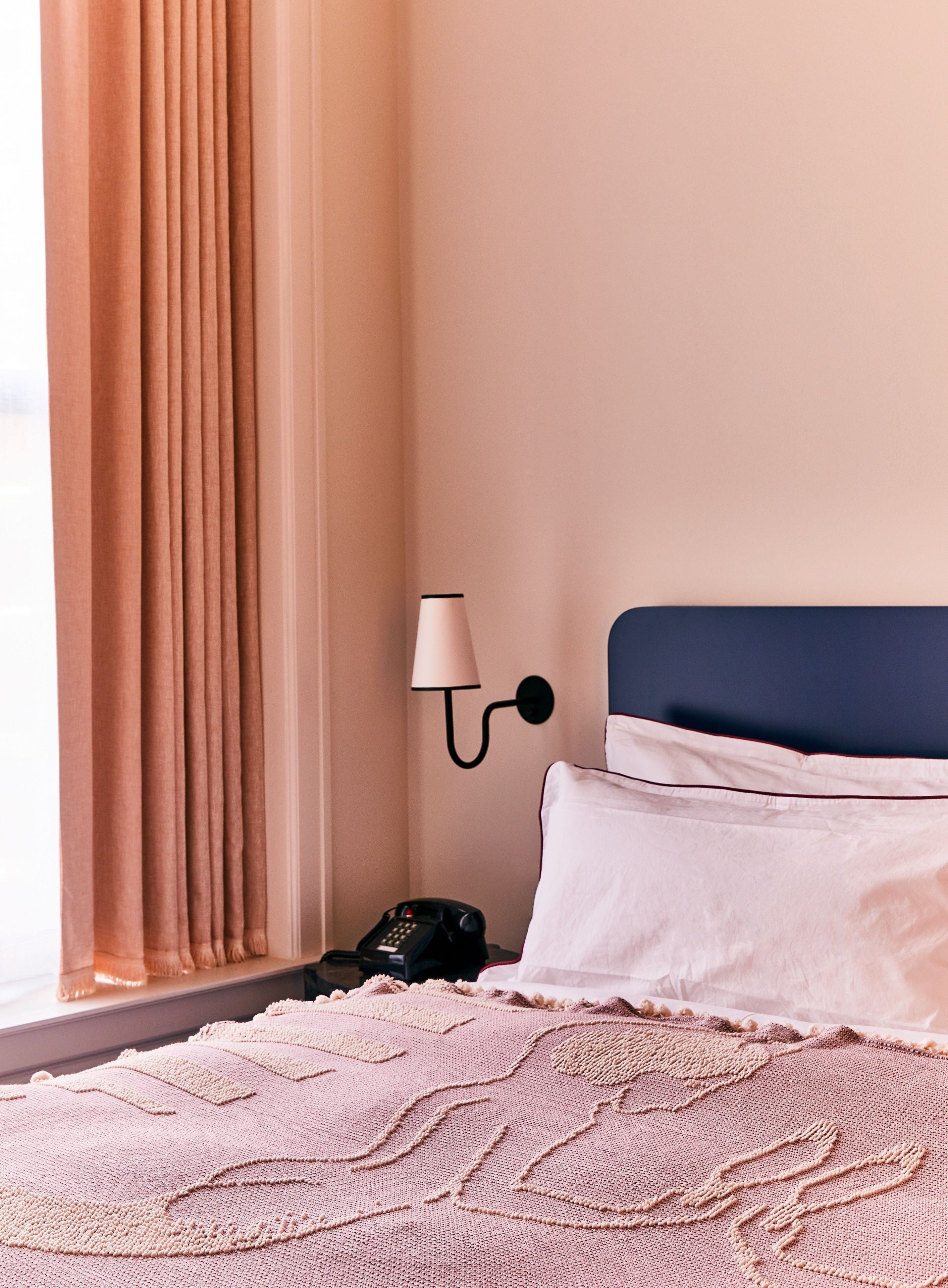 Un lit bien fait, avec un oreiller blanc et une tête de lit bleue, une lampe de chevet et un téléphone sur la table de chevet.