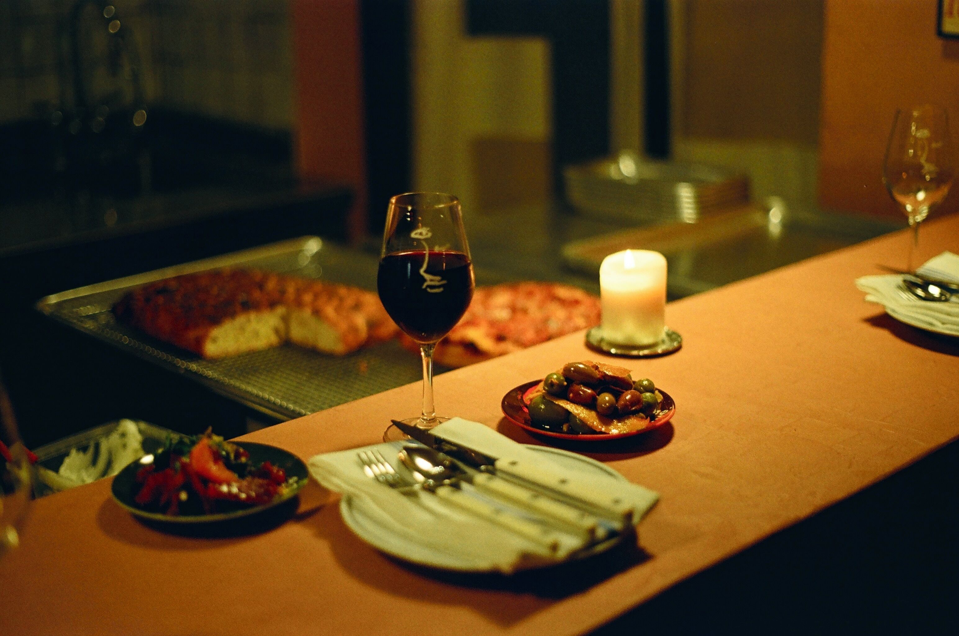 Une table à manger avec des assiettes, des couverts, un verre de vin rouge et une bougie.